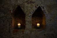 twee witte brandende kaarsen in twee nissen in een donkere oude bakstenen muur van een klooster, kop van Maren Winter thumbnail