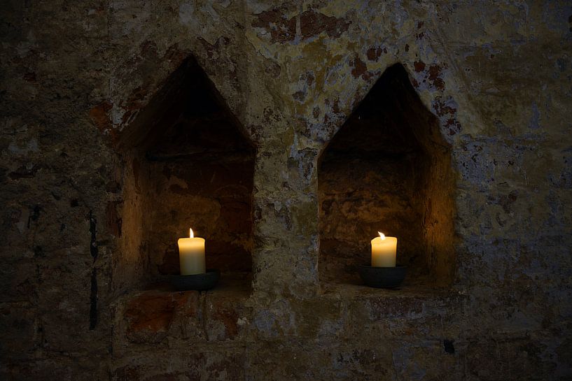 twee witte brandende kaarsen in twee nissen in een donkere oude bakstenen muur van een klooster, kop van Maren Winter