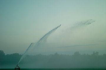 Een watersproeier irrigatie pistool sproeit water over een akker van John Quendag