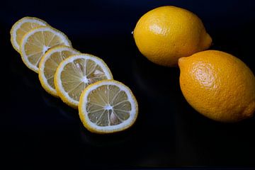 Zitrone als ganze Frucht und in Scheiben geschnitten auf schwarzem Servierteller