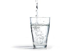 water wordt in een drinkglas gegoten, geïsoleerd op een witte achtergrond met kopieerruimte