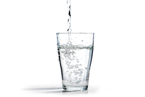 Wasser wird in ein Trinkglas gegossen, isoliert auf weißem Hintergrund mit Kopierraum