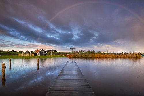 Een mooie regenboog tijdens de zonsopkomst boven het Lauwersmeer in Friesland. In de lucht drijven m