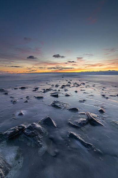 De pier komt langzaam tevoorschijn wanneer de zee zicht terugtrekt tijdens een kleurrijke zonsondergang van Bram Lubbers