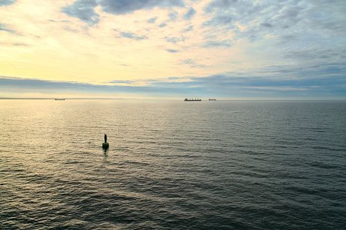 Groene boei in de kalme zee bij zonsopgang, schepen aan de horizon en een dramatische lucht