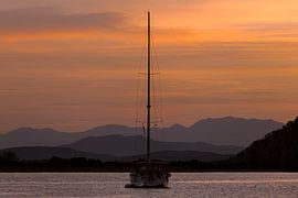 Segelboot mit den Bergen von Kefalonia im Hintergrund im Kontrast zum schönen Morgenlicht. von Stef Heijenk