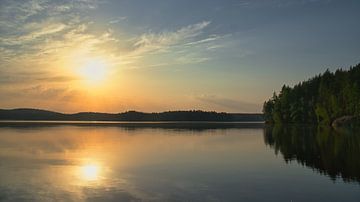 Gouden zonsondergang boven een rustig bosmeer in Scandinavië.
