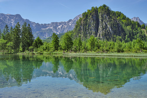 An alpine lake in which green trees and the bright blue sky are reflected