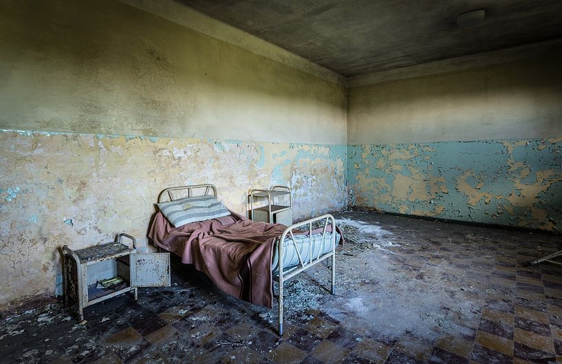 Bed with bedside table in an abandoned care facility by Inge van den Brande