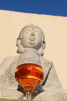 Buddha met een wijnglas tegen muur en felblauwe lucht