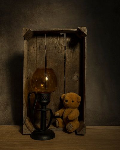 still life with old teddy bear and a golden light in an old wooden box on a table with dark backgrou