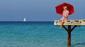 Young woman with umbrella looking out to sea by Matthias Stolt