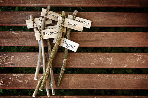 kreative Pflanzenmarker auf einem Holztisch, beschriftet mit Kräuternamen für den ländlichen Garten,