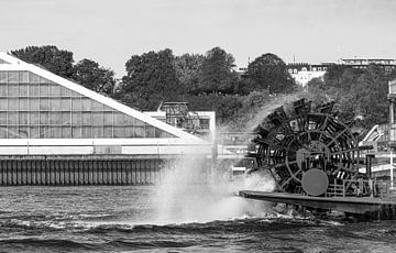Wiel van een raderstoomboot die water spuit voor het gedeeltelijk zichtbare dok in Hamburg van Andrea Gaitanides - Fotografie mit Leidenschaft
