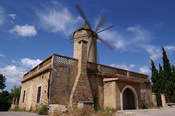 Stone house with windmill in front of blue sky with clouds