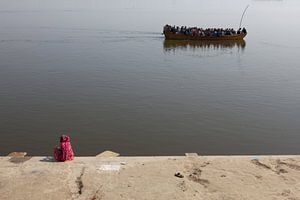 Indian woman on the banks of the Ganges in Varanasi watches a passing boat carrying Hindustani by Wout Kok