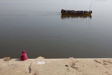 Indische Frau am Ufer des Ganges in Varanasi beobachtet ein vorbeifahrendes Boot mit Hindustani