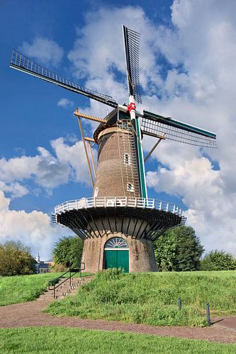 Traditionele Nederlandse windmolen op een dijk tegen een zonnige blauwe hemel