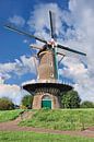 Traditionele Nederlandse windmolen op een dijk tegen een zonnige blauwe hemel van Tony Vingerhoets thumbnail