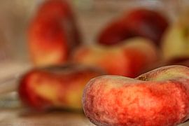 A flat peach in front of a bowl of other fruit by Photoart-Naegele