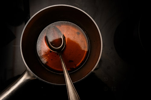 Topf und Löffel mit Rinderbrühe beim Kochen einer Rotwein-Morchelsauce auf einem schwarzen Herd, dun