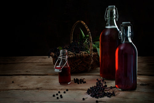 hausgemachter Saft aus schwarzen Holunderbeeren (Sambucus nigra) in Flaschen und Beeren in einem Kor