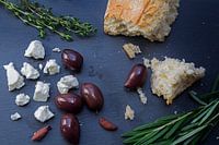 Kalamata-Oliven und Feta-Käse aus Griechenland mit Brot und Kräutern auf dunklem Schiefergrund