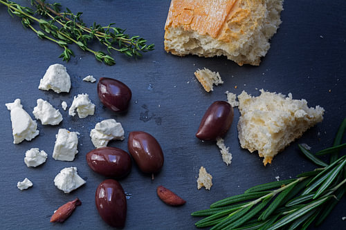 Kalamata-Oliven und Feta-Käse aus Griechenland mit Brot und Kräutern auf dunklem Schiefergrund