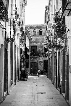 Eine Frau geht eine leere Straße in einem typischen Mittelmeerdorf entlang. von Arte D'España