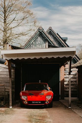 A bright red vintage sports car, identified as a Fiberfab FT Bonito, parked head-on under a wooden carport.