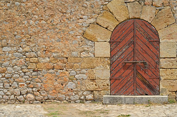An old brown wooden arched door set in a stone wall