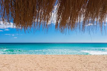 Beautiful sand beach with turquoise sea water, sun, blue sky and straw umbrella