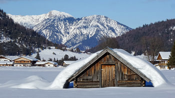 Schneebedeckte Hütte vor Bergen und blauem Himmel bei Krün