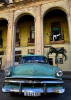 Groene oldtimer voor geel gebouw in Havana, Cuba