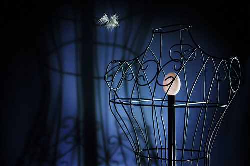Ei in einer Metallschneiderpuppe wie in einem Vogelkäfig und einer fliegenden Feder, surreales Kunst