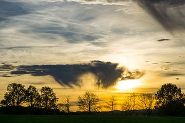 Oranje lucht met dramatische wolken als zonsondergang op landschap met brede weide van adventure-photos