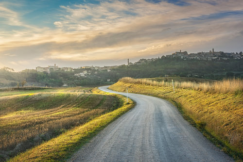 Landweg bij zonsopgang met de skyline van Montepulciano en wijngaarden