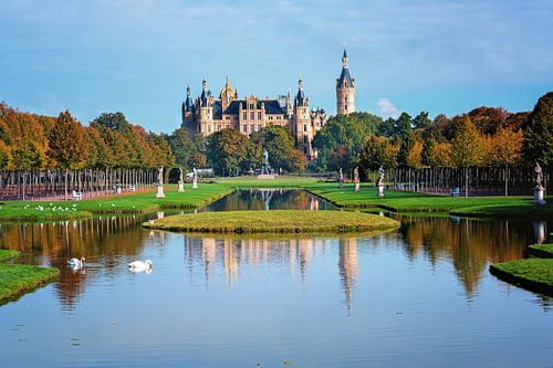 Schweriner castle seen from the park with water canals, reflections, sculptures and trees with color