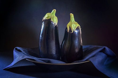 Two eggplants standing on a plate with a dark blue napkin agains