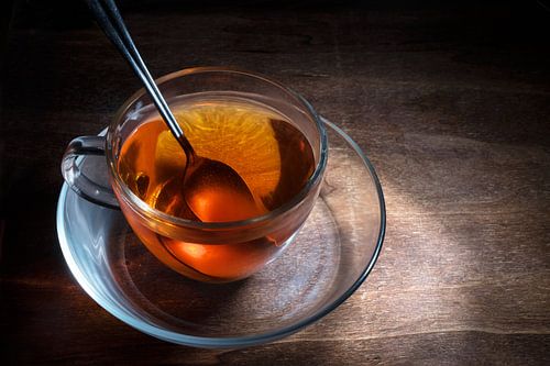 black tea freshly brewed in a glass cup and a spoon on a dark rustic wooden table, steaming hot drin