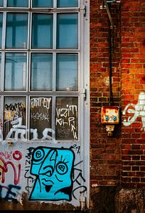 Industriefenster & Graffiti‑Gesicht – Backsteinwand mit rostigem Schaltschrank | urbane Wandkunst