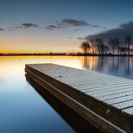 Besneeuwde steiger en bomenrij reflecteren in het rustige meer tijdens zonsopkomst van Bram Lubbers