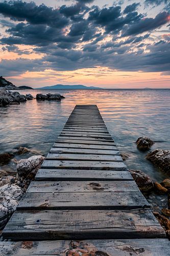Houten steiger leidt naar rustig zee bij zonsondergang