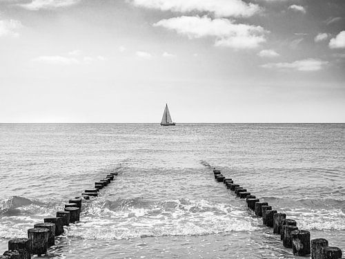 Zeilboot tussen strandpalen in Zeeland, zwart-wit