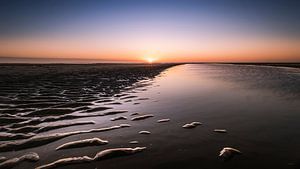 Strukturen im Sand, Wasser und eine untergehende Sonne
