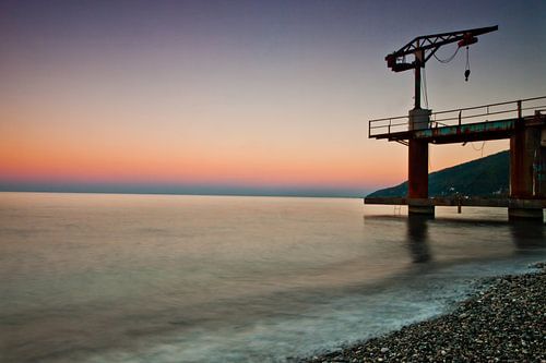 Sunset over the sea, purple and pink colors, a small crane on the pier