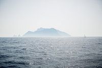 A sailboat sails off an island on the Amalfi coast in Italy