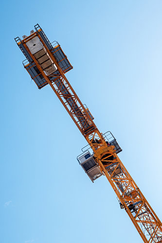 Detail eines Krans vor blauem Himmel, orangefarbene Metallkonstruktion und Betongewichte, Kopierraum