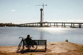 Cyclist on Bench by Shimmering Water — Bridge Under Construction