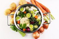 Bouillon met wortelen, uien, diverse verse groenten in een pot - kleurrijke verse heldere lentesoep.